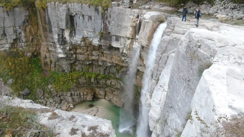 Travelers looking at Kinchkha waterfall cascading into a natural pool