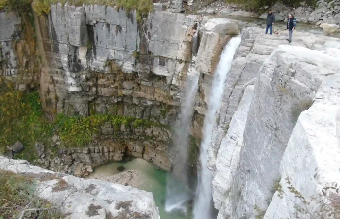Travelers looking at Kinchkha waterfall cascading into a natural pool