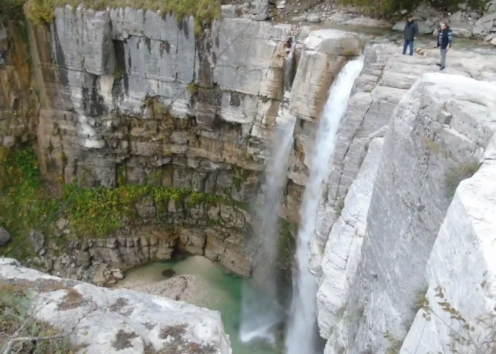 Travelers looking at Kinchkha waterfall cascading into a natural pool