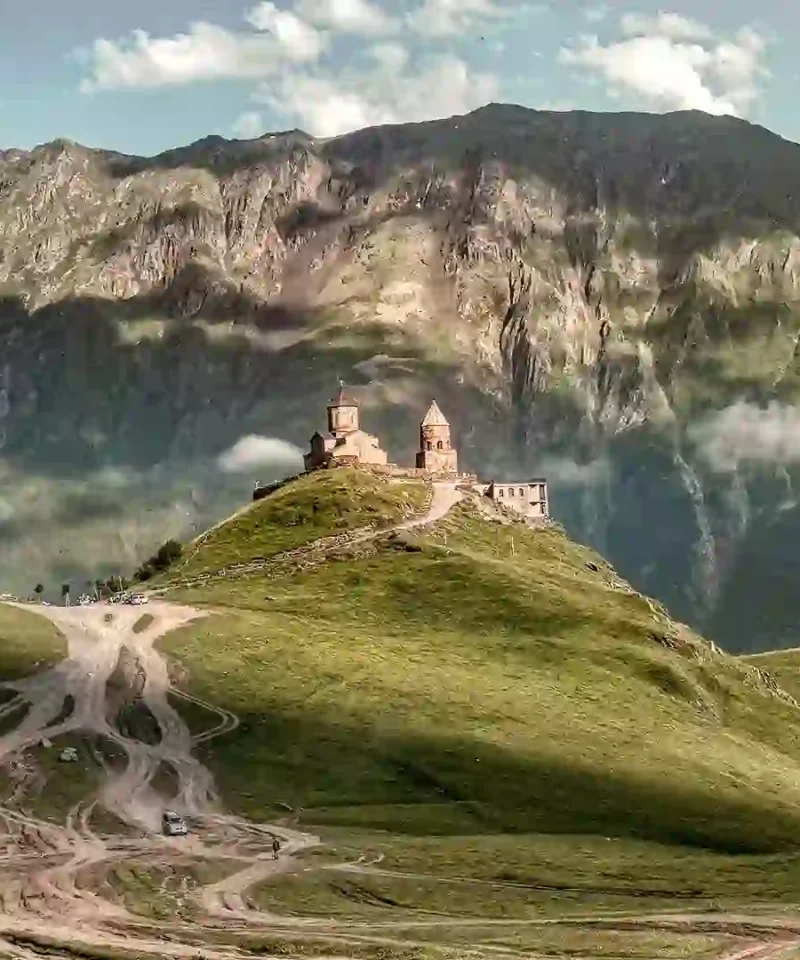Gergeti Trinity Church in Kazbegi with mountain roads and paths under a cloudy sky.