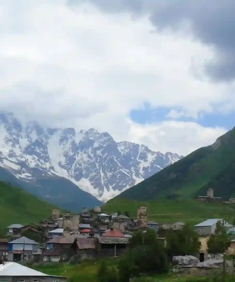 Ancient stone defense towers in Ushguli village with the massive snowy peak of Mount Shkhara in Svaneti Georgia